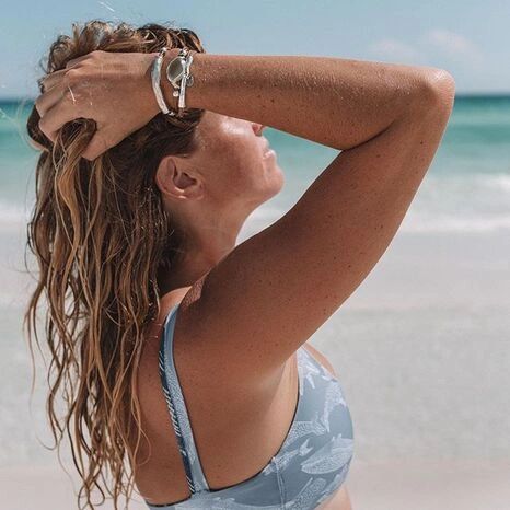 Woman in a patterned bikini top enjoying the beach with her hand in her hair.