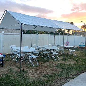 Outdoor canopy with white tables and chairs at sunset.