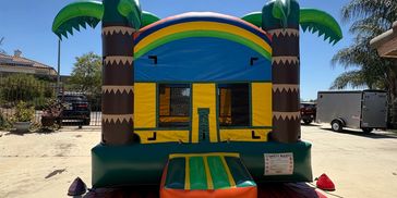 Bright inflatable bounce house with palm trees and a rainbow design.