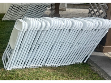 Stack of white folding chairs arranged outdoors on grass.