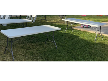 Two white folding tables set up on green grass outdoors.