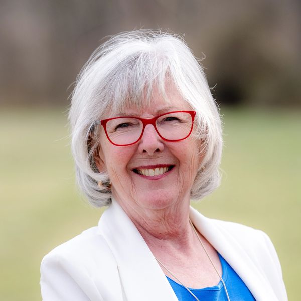 Smiling elderly woman with white hair and red glasses outdoors.
