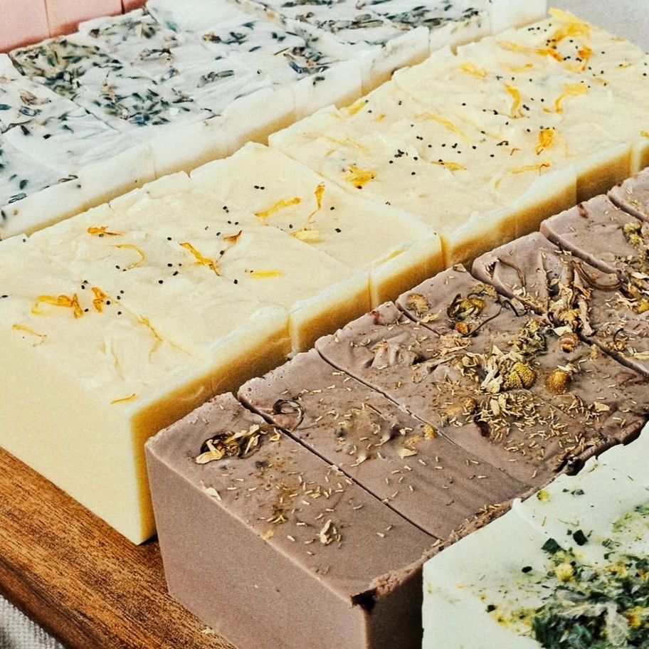 Rows of artisanal soaps with natural herbs and flowers on top.