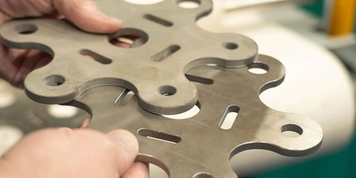 Hands holding two intricately shaped metal plates with cutouts.