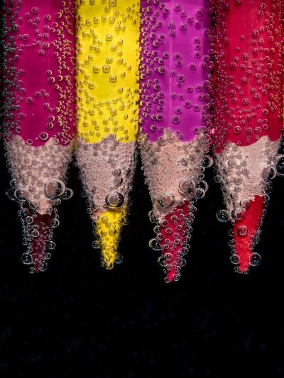 Colored pencils submerged in water with bubbles forming on them.