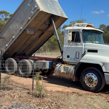 White dump truck unloading dirt in a rural area.