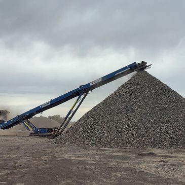 Large conveyor belt piling up gravel under a cloudy sky.