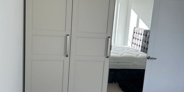 A beige wardrobe with a mirrored door in a bright bedroom.
