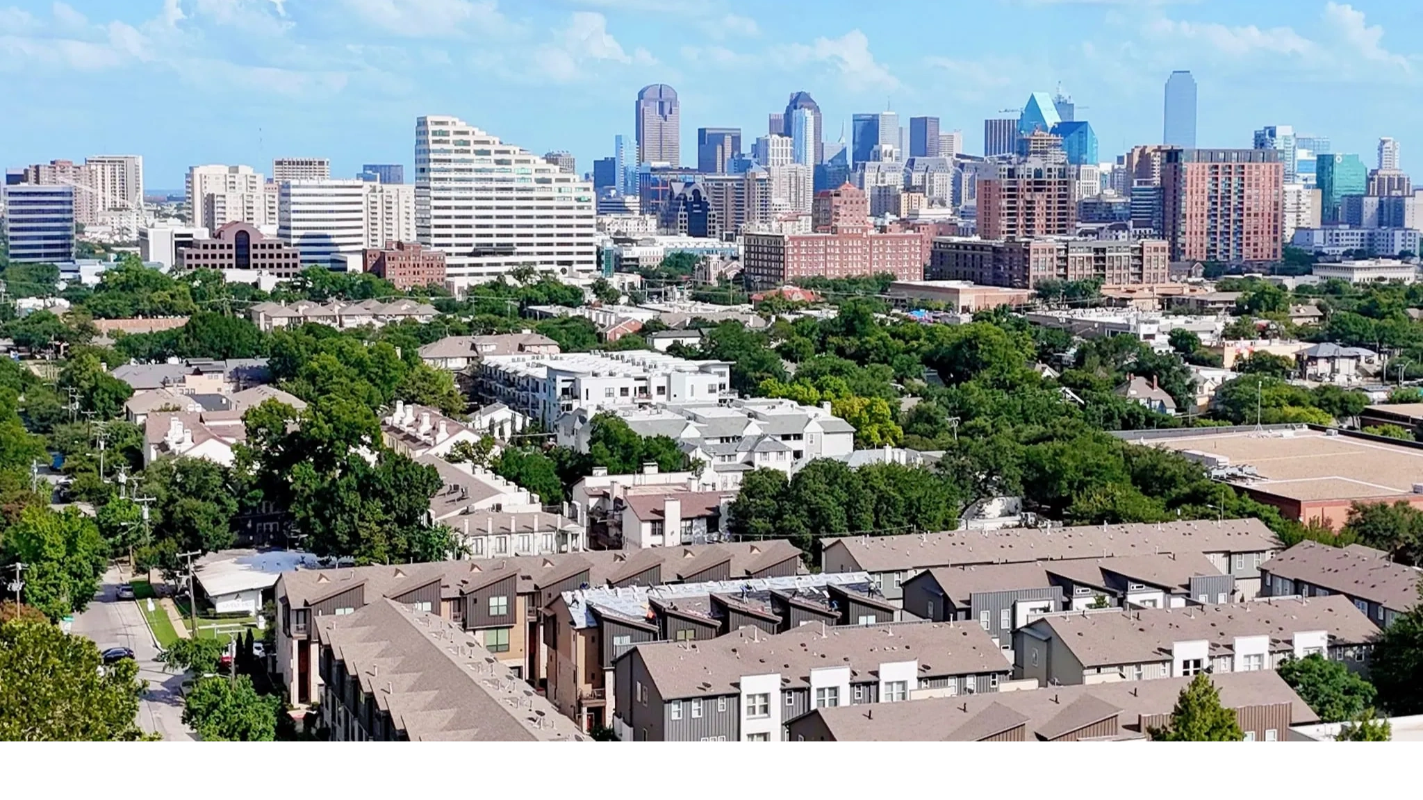 A vibrant cityscape with modern buildings and lush green trees under a clear blue sky.