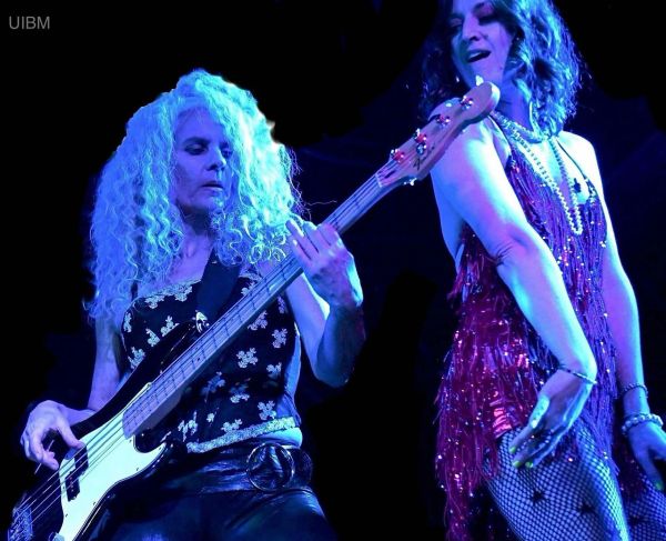 Two women performing on stage, one playing bass guitar.