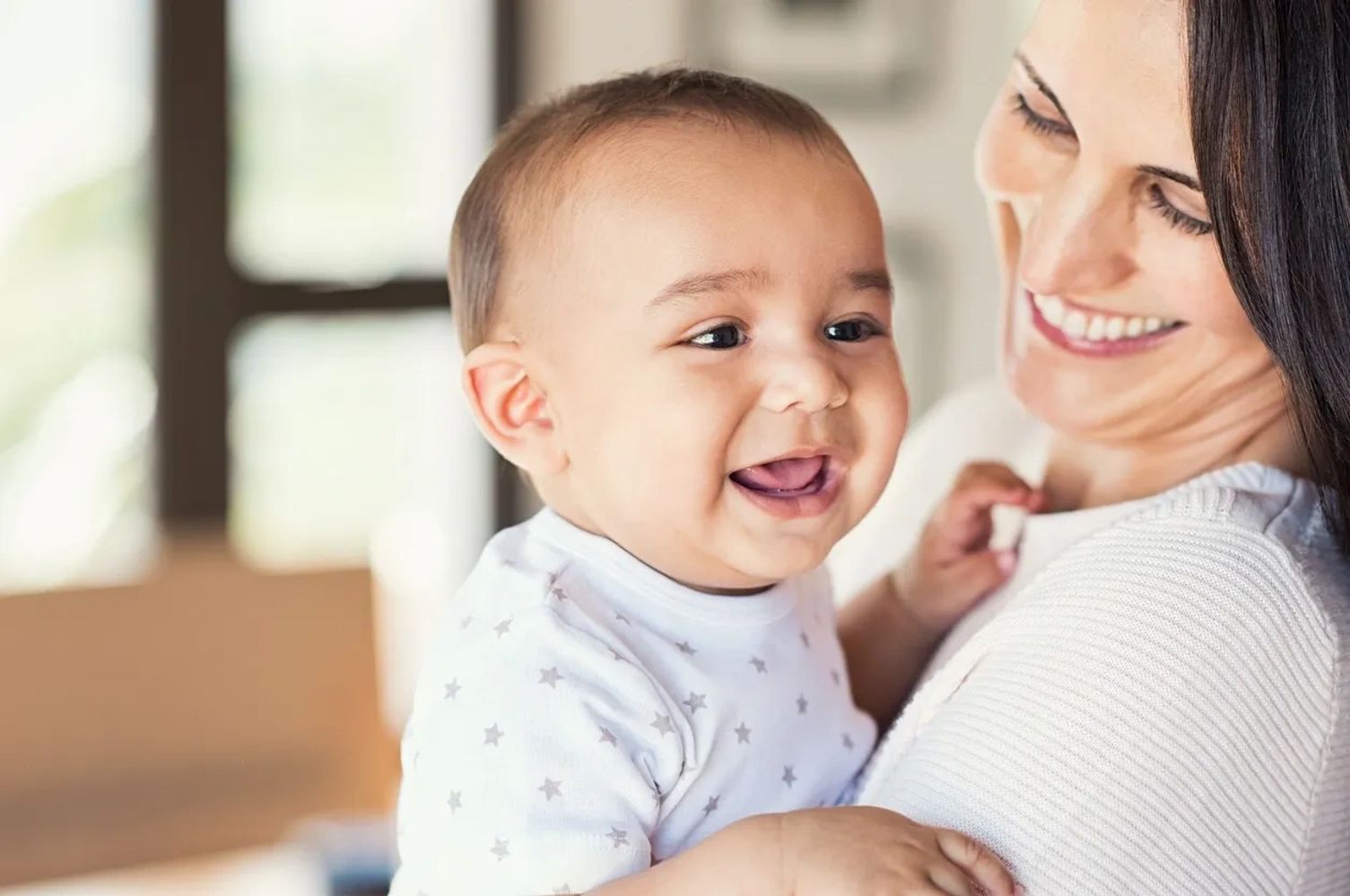 A mother holding her baby, both smiling.