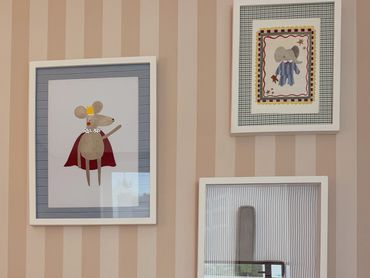 Framed cartoon mice art on striped wallpaper in a cozy room.