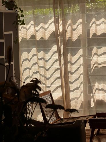 Sillón de mimbre iluminado por la luz solar detrás de una cortina.