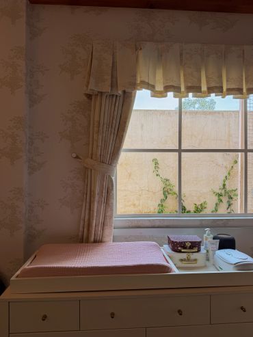 Mesa blanca para cambiar a bebé junto a ventana con cortinas.