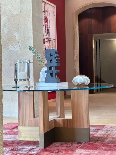 Modern glass table with wooden base and decorative items on a red rug.