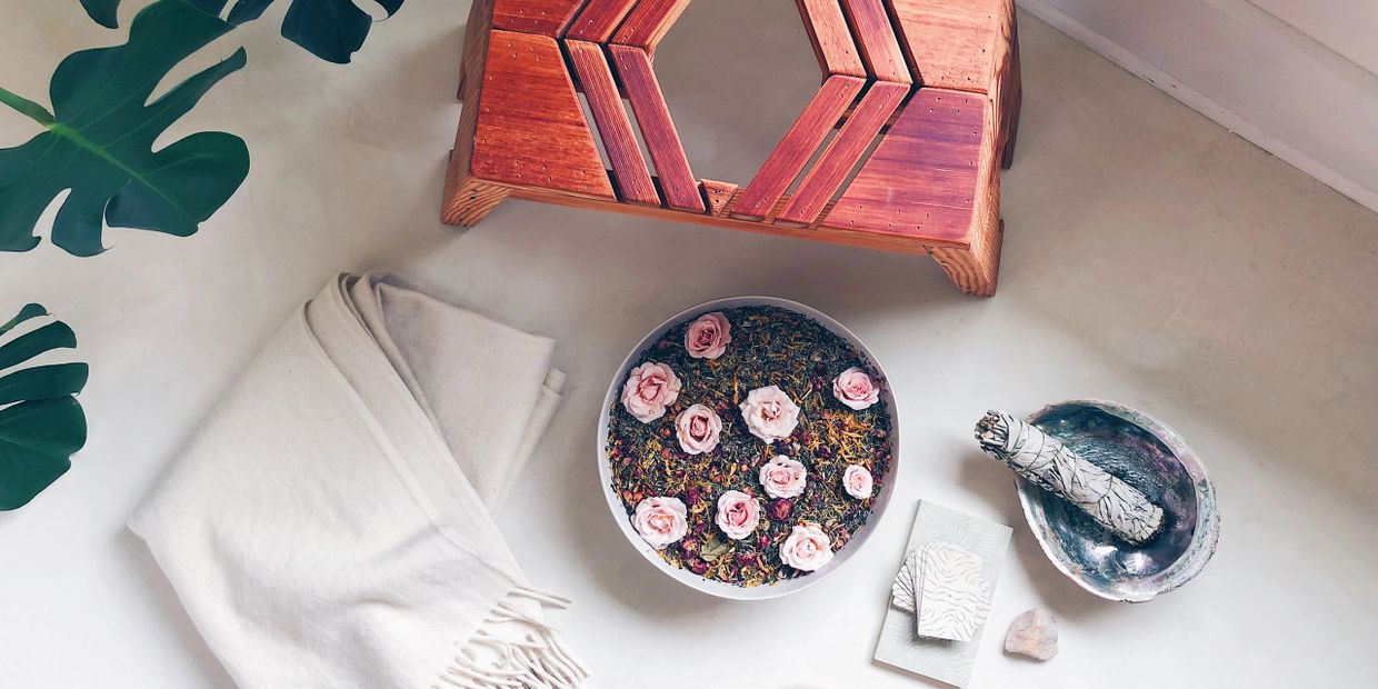 Cozy arrangement with a white blanket, dried flowers, and smudge stick on a white surface.