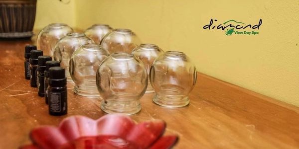 Glass cupping jars and essential oil bottles lined up on a wooden surface at a spa.