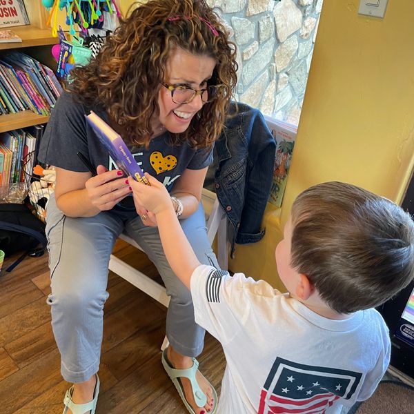 A woman joyfully interacts with a young boy, holding a book in a cozy room.