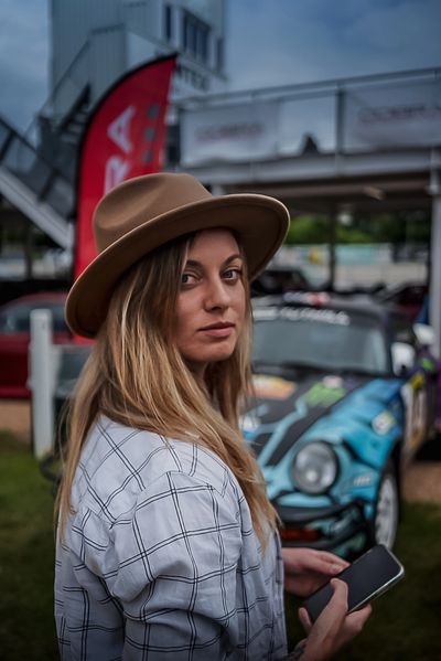 Woman in a brown hat holding a phone, standing near a painted car.