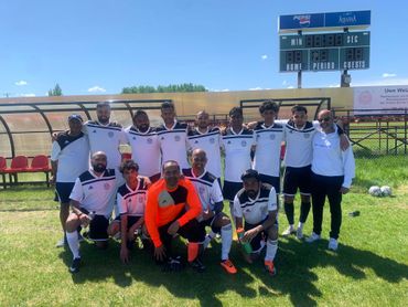 Soccer team posing together on a sunny field with scoreboard in background.