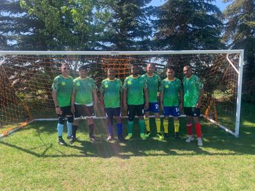 Seven soccer players pose in front of a goal on a sunny field.