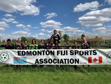 Edmonton Fiji Sports Association team posing with trophy behind a banner outdoors.