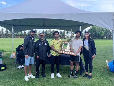 Group of five people holding a large trophy under a canopy outdoors.