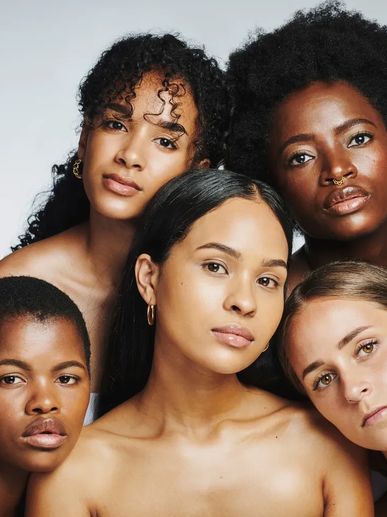 A diverse group of five women posing closely together against a plain background.