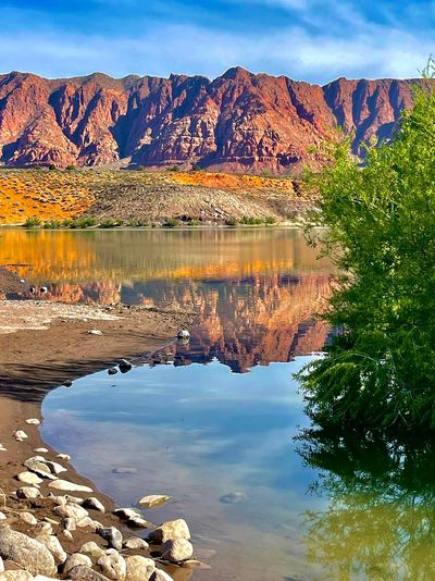 A serene lake reflecting red rocky mountains under a clear blue sky.