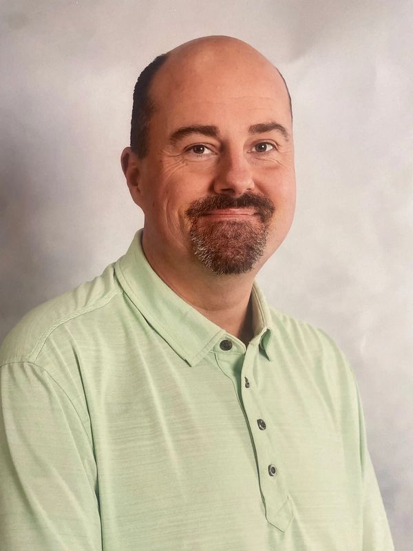 Smiling man with a goatee wearing a light green collared shirt.