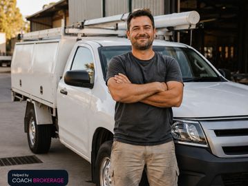 Confident tradesperson arms crossed beside white work ute, helped by Coach Brokerage badge