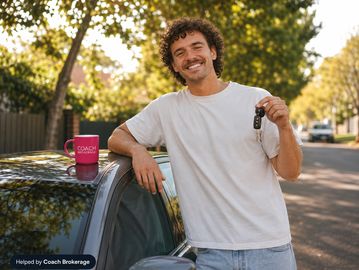 Young man with car keys beside his new car, Coach Brokerage mug on roof, sunny suburban street