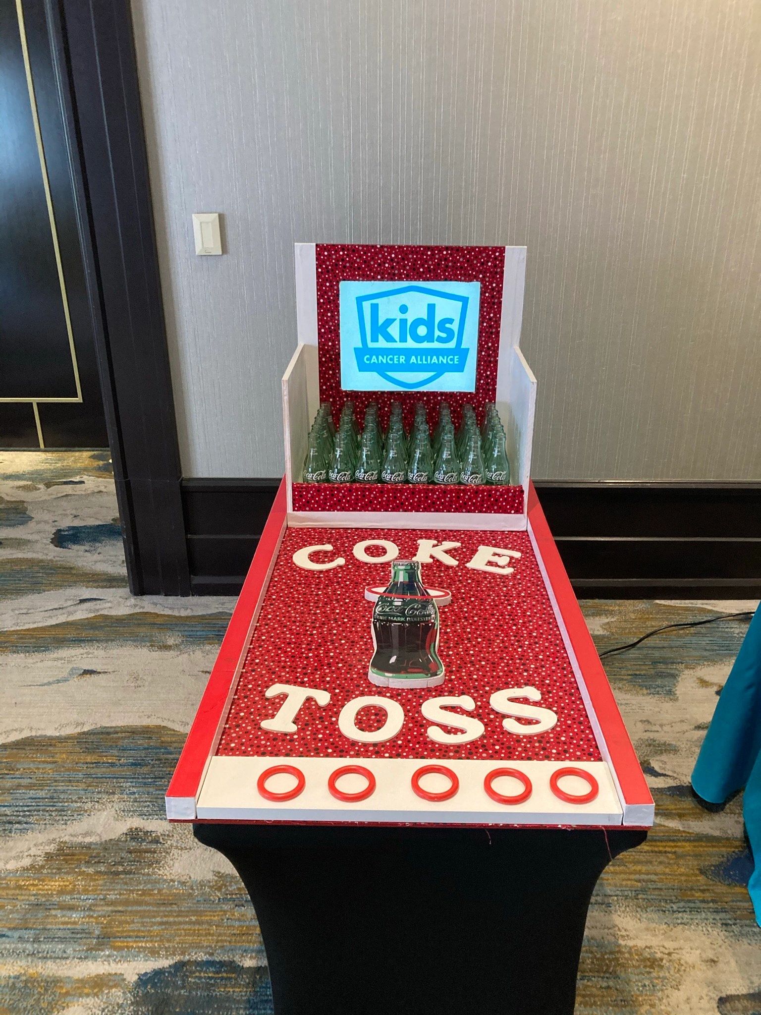 Coke Toss carnival game with bottle targets and a themed display, an example of a game rental attraction.