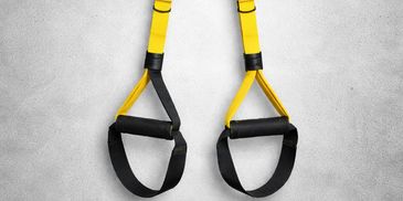Yellow and black suspension training straps hanging against a grey wall.