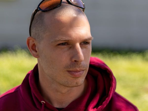 Man in a red hoodie with sunglasses on his head looking to the side.