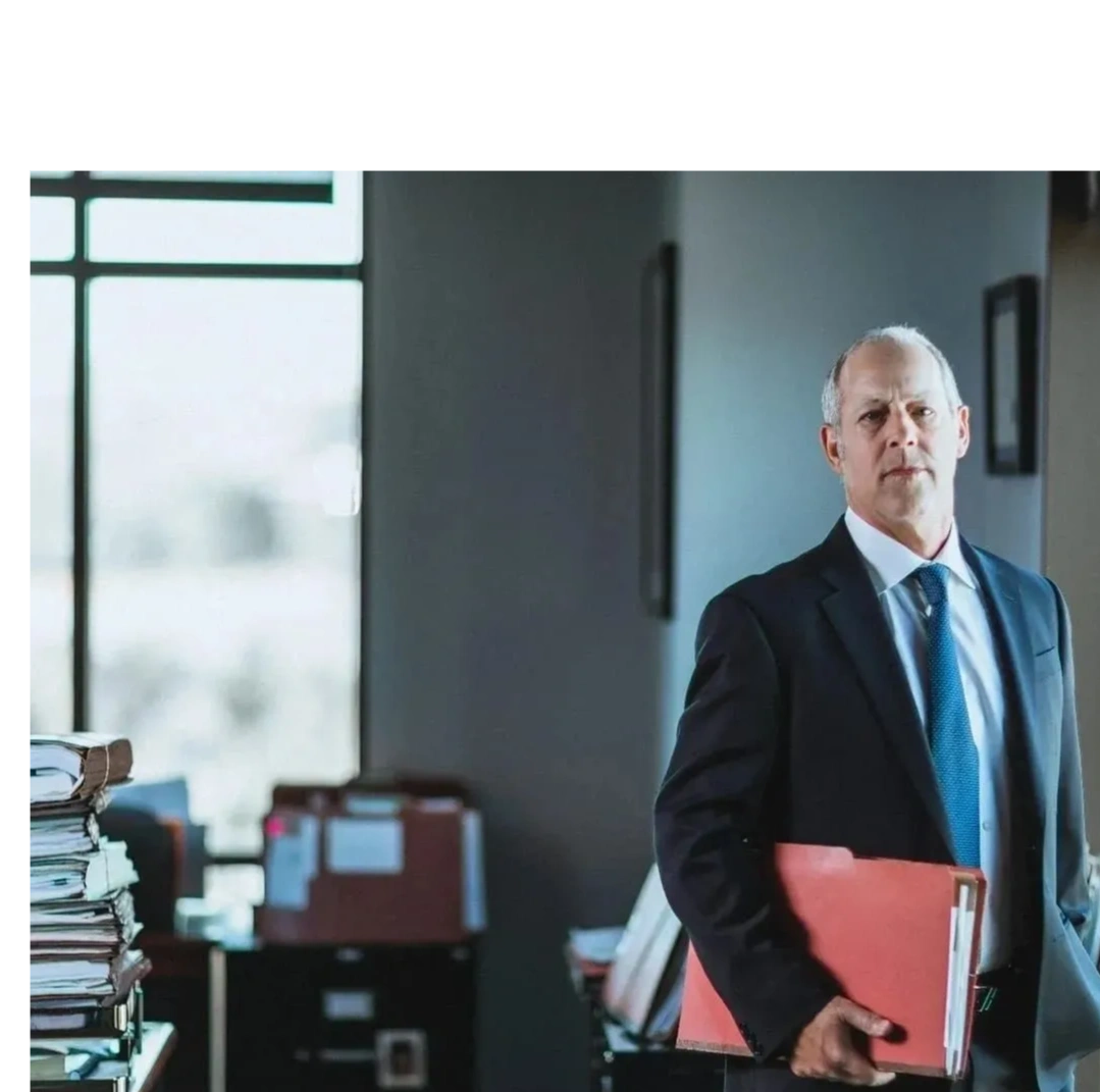 Middle-aged businessman holding a red folder in a dimly lit office.