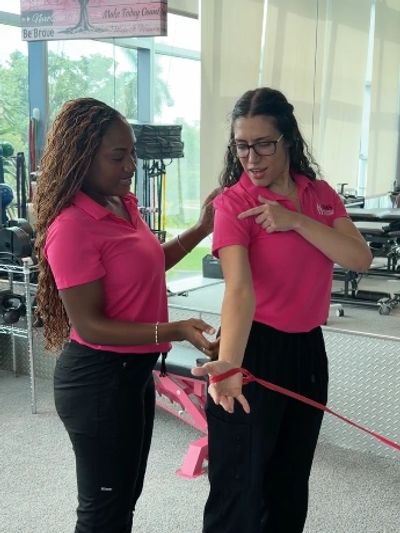 Two women exercising with a resistance band in a gym.
