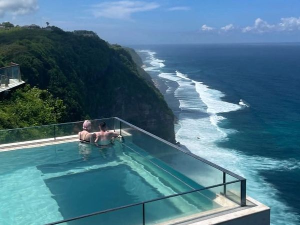 Couple enjoying an infinity pool overlooking a cliff and ocean.