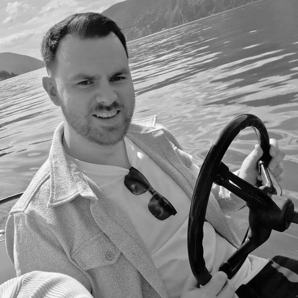 Man smiling while steering a boat on a lake.