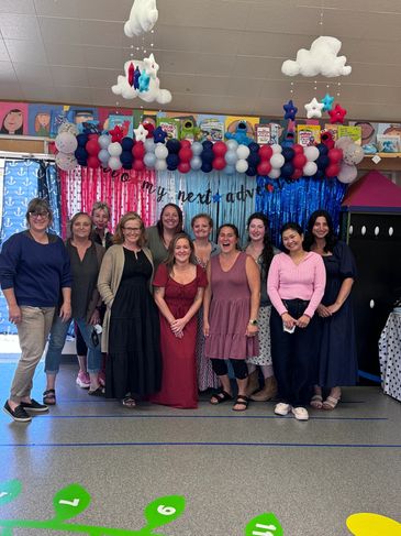 Group photo of smiling adults with a festive balloon arch.
