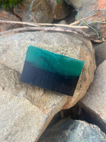 A rectangular green and black stone resting on natural rocks.