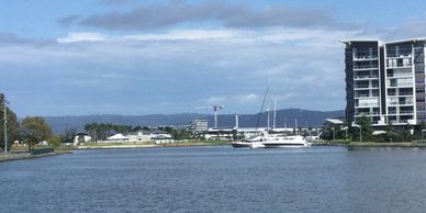 Boats docked near modern buildings along a calm waterfront on a partly cloudy day.