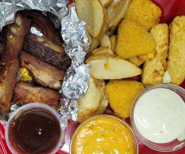 A platter with grilled ribs, potato wedges, cheese dip, ranch sauce, and fried snacks.