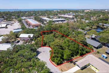 Aerial view of a green plot of land outlined in red in a neighborhood.