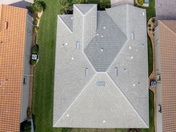Aerial view of a large gray roof between two tan-roofed houses.