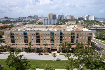 Large beige apartment building with balconies and palm trees in front.