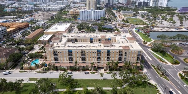 Aerial view of a large residential building with a pool and surrounding greenery in an urban area.