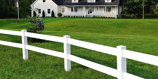 White fence in front of a large house with green lawn.