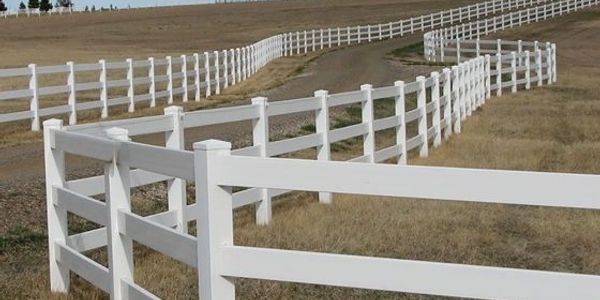 White fence lining a winding dirt road in a field.