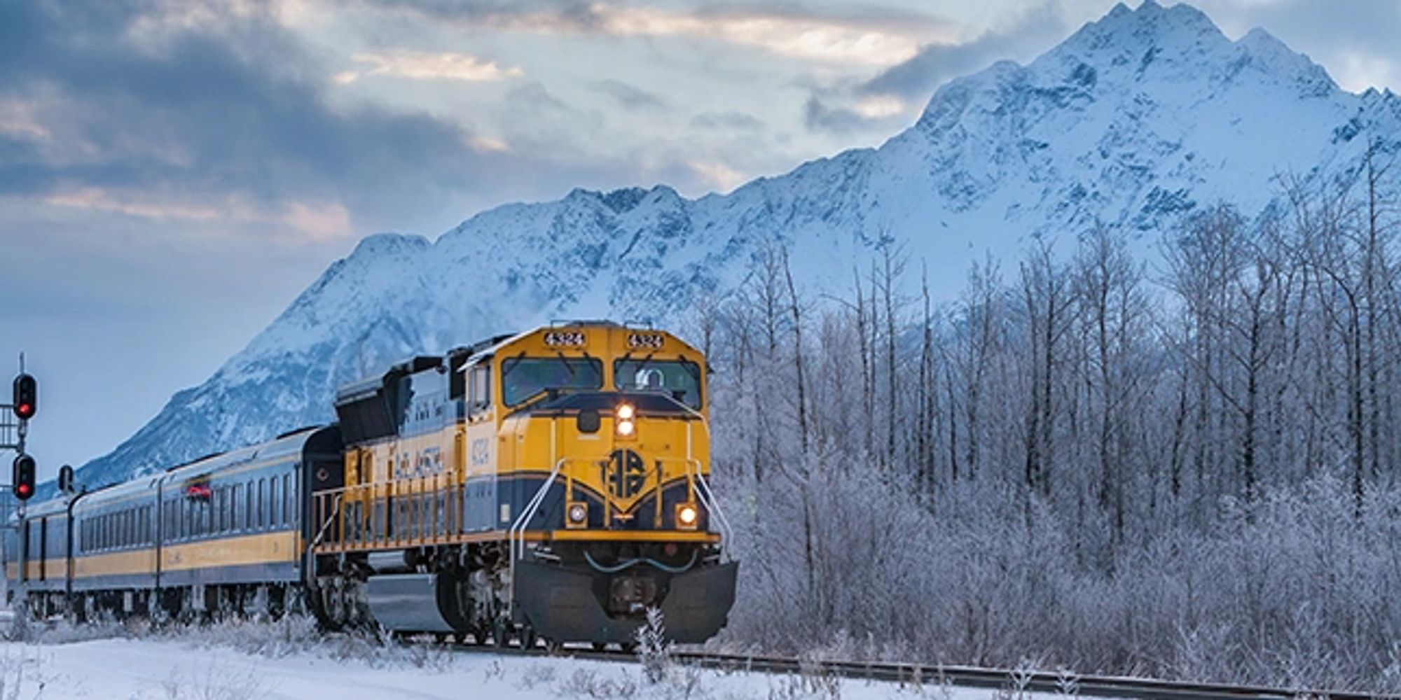 Yellow and blue train traveling through snowy landscape with mountains.